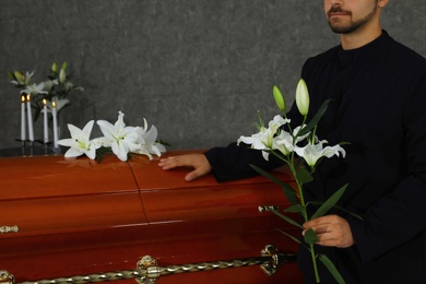 Young man with white lilies near casket in funeral home, closeup