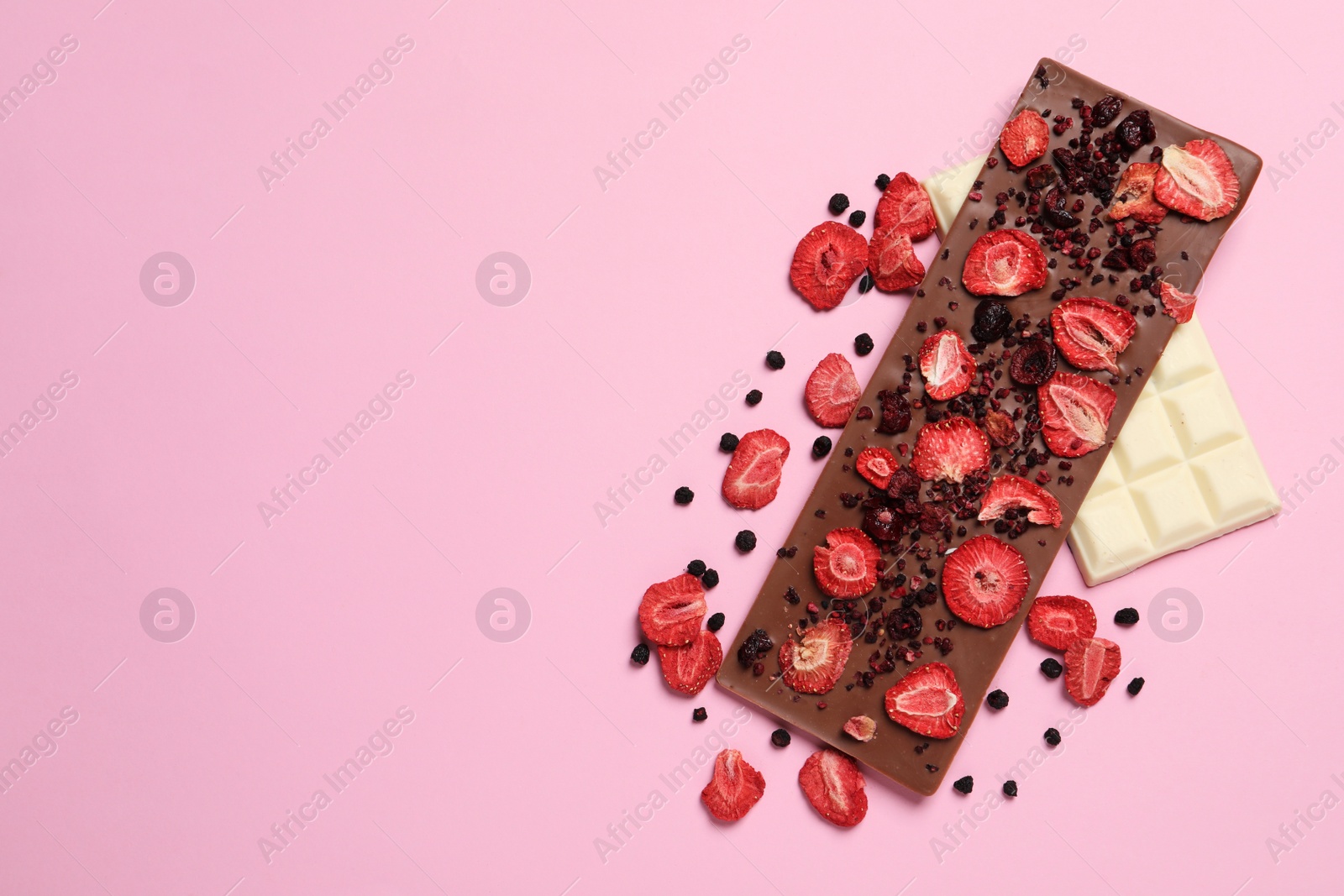 Photo of Chocolate bars with freeze dried fruits on pink background, flat lay. Space for text