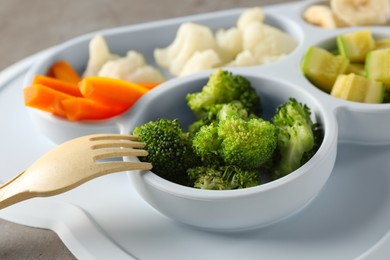 Photo of Baby food. Section plate with different vegetables served on grey textured table, closeup