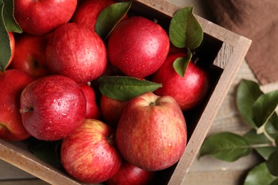 Crate with wet red apples and green leaves on table, top view