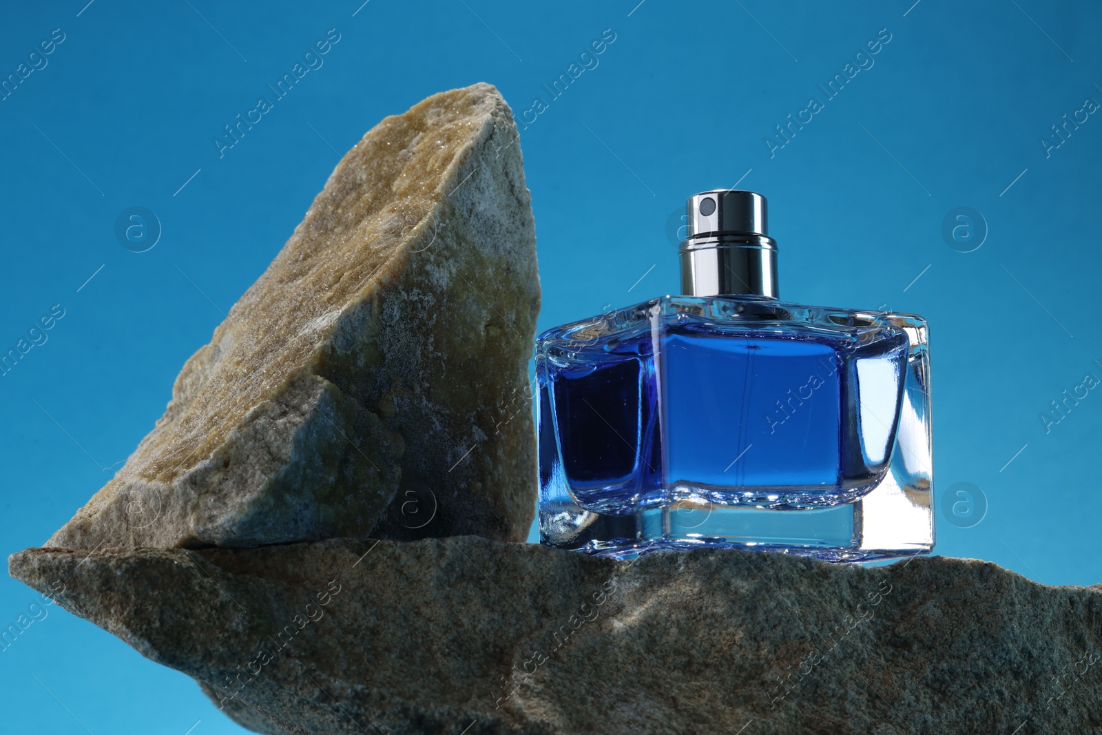 Photo of Stylish presentation of luxury men`s perfume on stones against light blue background