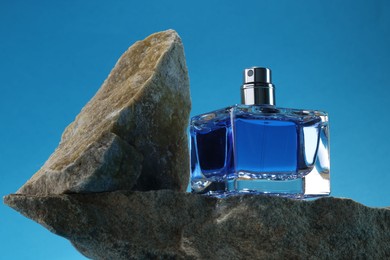 Photo of Stylish presentation of luxury men`s perfume on stones against light blue background