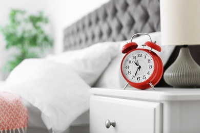 Photo of Analog alarm clock on table in bedroom. Time of day