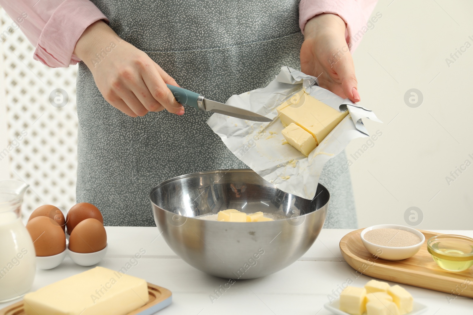 Photo of Woman adding fresh butter into bowl at white wooden table, closeup