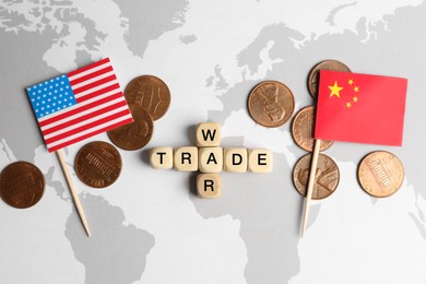 Phrase Trade war made with wooden cubes, coins near USA and China flags on world map, flat lay