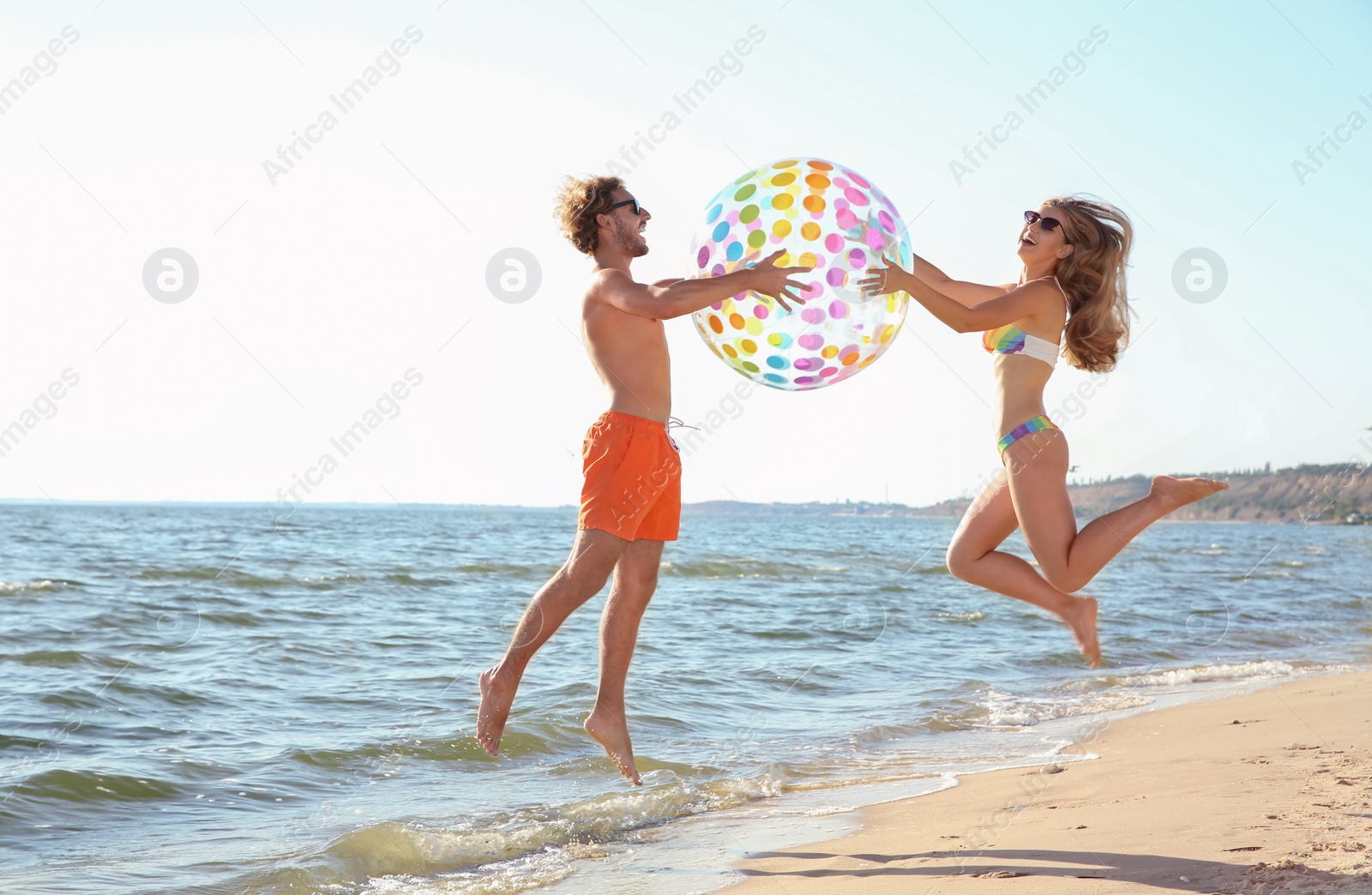 Photo of Happy young couple in beachwear jumping with inflatable ball on seashore