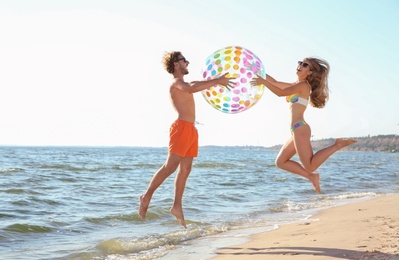 Photo of Happy young couple in beachwear jumping with inflatable ball on seashore