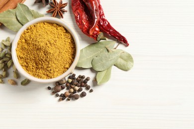 Photo of Curry powder in bowl and other spices on white wooden table, flat lay. Space for text