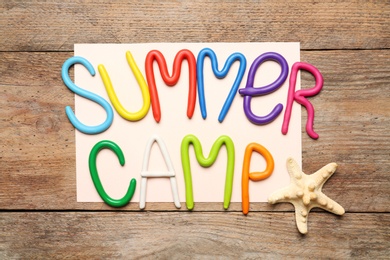 Photo of Text SUMMER CAMP made of modelling clay and starfish on wooden table, flat lay