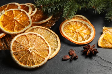 Photo of Dry orange slices, anise stars and fir tree branches on black table, closeup