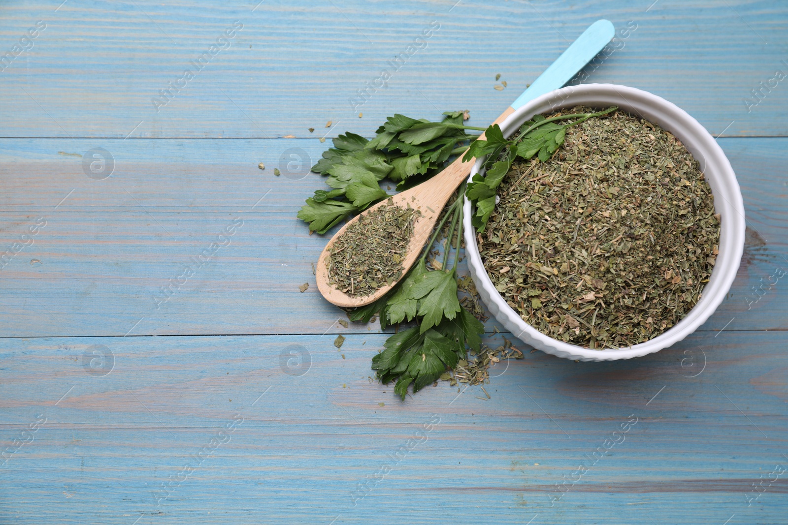 Photo of Dried parsley and fresh leaves on light blue wooden table, flat lay. Space for text
