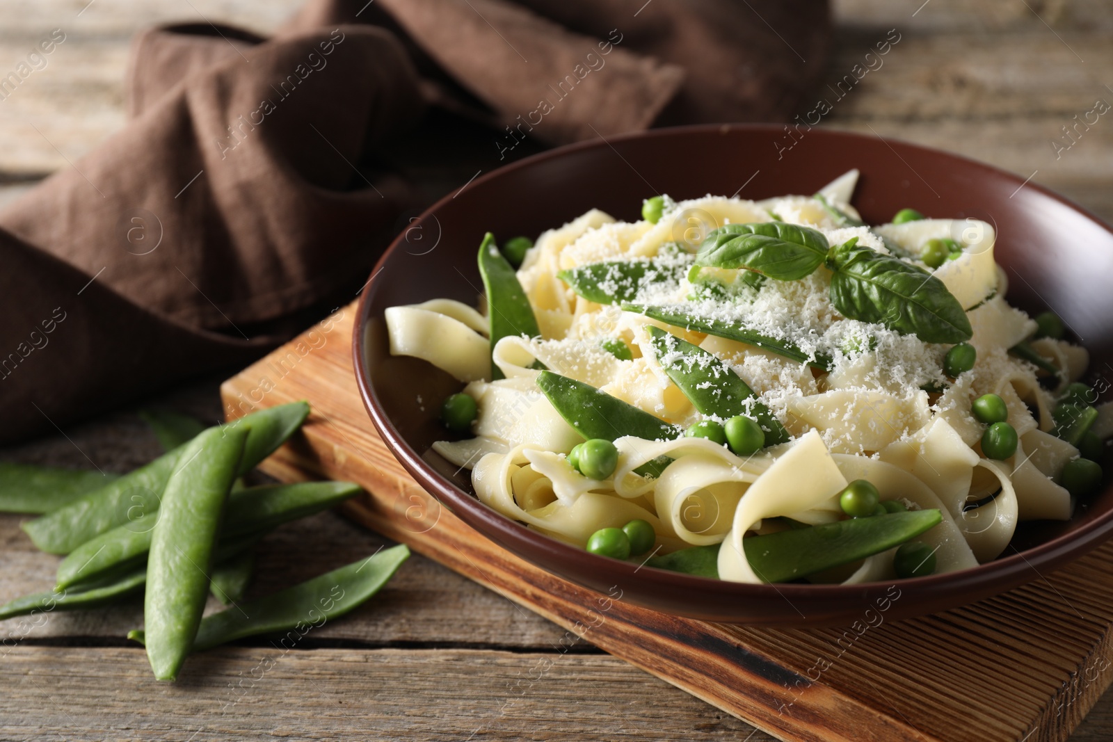 Photo of Delicious pasta with green peas, fresh basil and cheese on wooden table, closeup