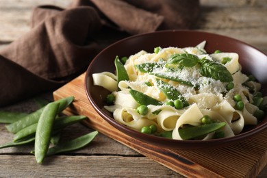 Photo of Delicious pasta with green peas, fresh basil and cheese on wooden table, closeup