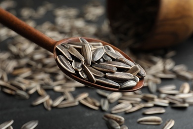 Photo of Spoon with organic sunflower seeds over grey table, closeup