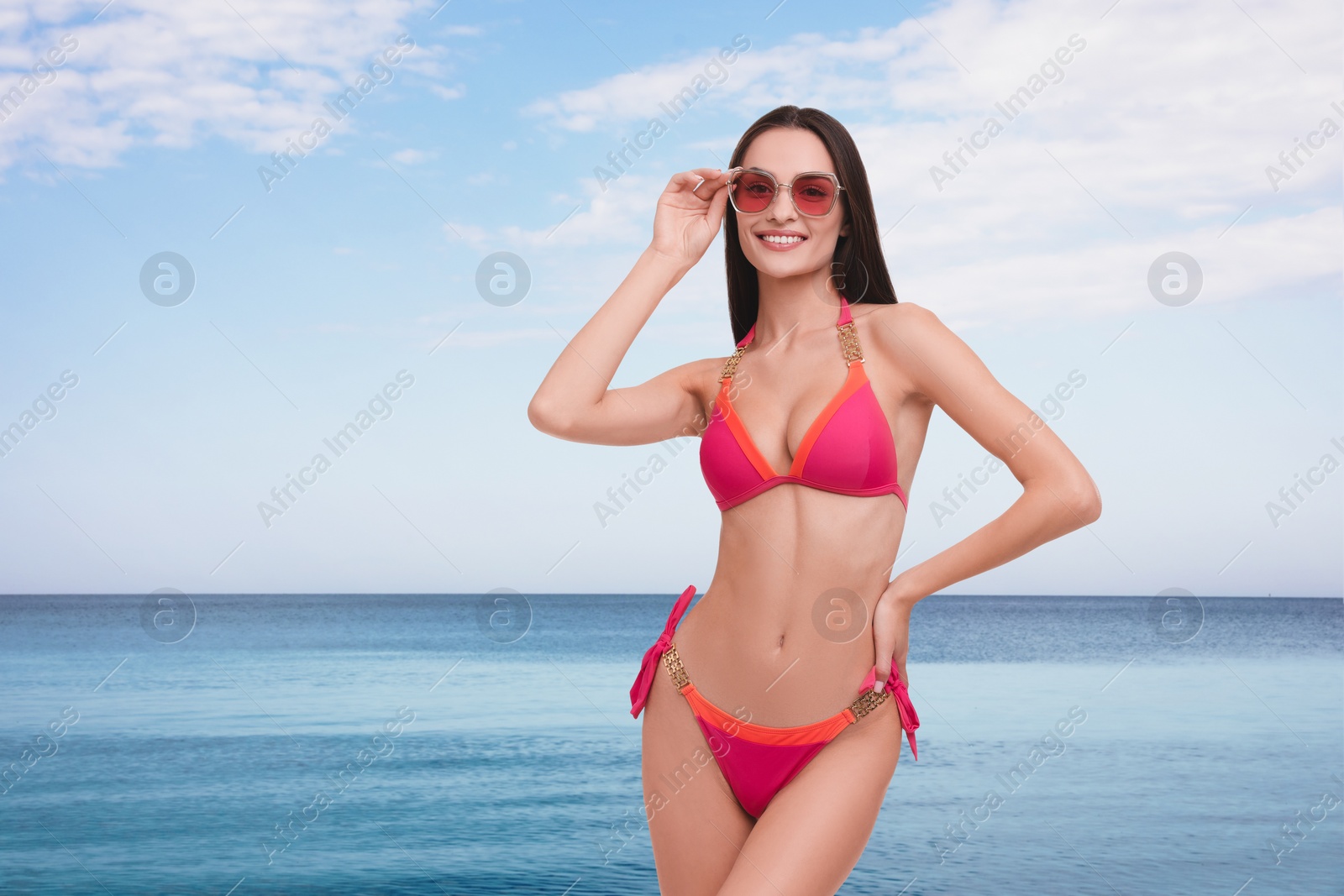 Image of Happy woman in stylish pink bikini and sunglasses near sea, space for text