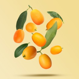 Image of Delicious fresh kumquats and green leaves falling on beige background