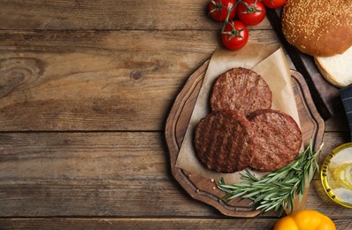 Photo of Tasty grilled hamburger patties, vegetables, rosemary and bun on wooden table, flat lay. Space for text