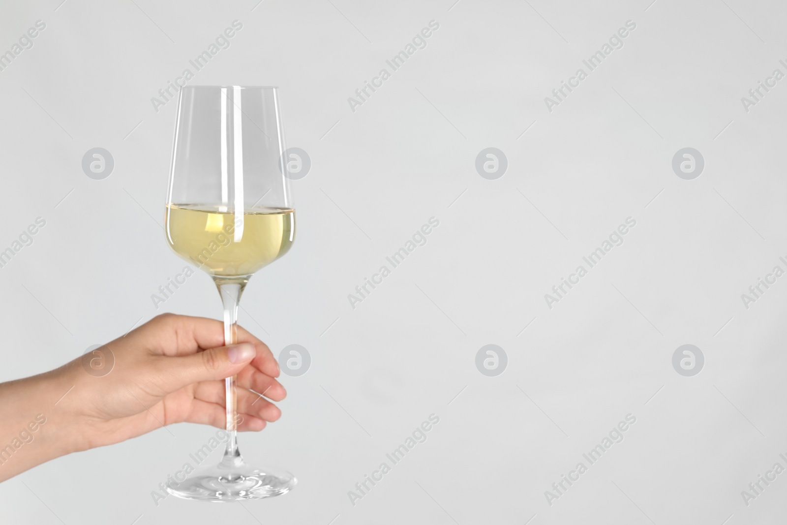 Photo of Woman holding glass of white wine on light background, closeup. Space for text