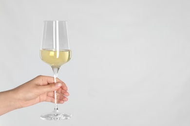 Woman holding glass of white wine on light background, closeup. Space for text