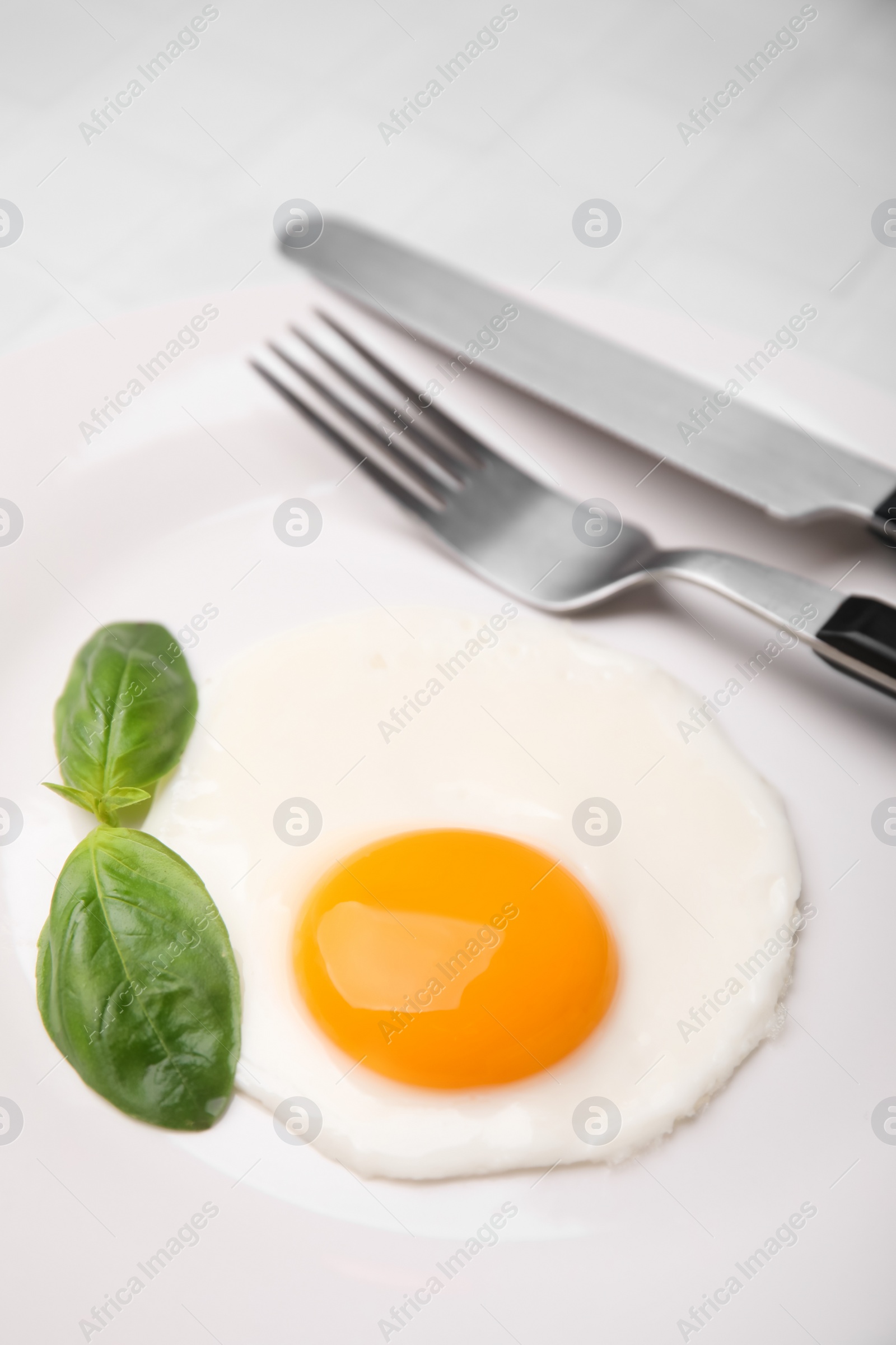 Photo of Tasty fried egg with basil in plate on white table, closeup