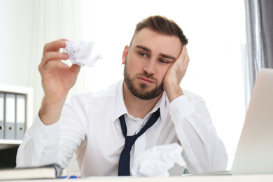 Photo of Lazy young man with crumpled paper at messy table in office