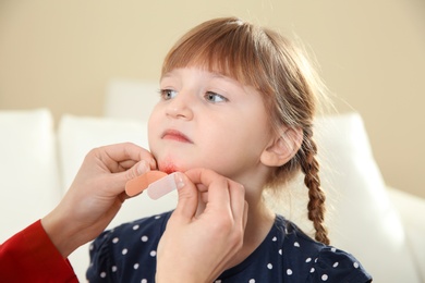 Nurse applying medical patch to little girl's injured face indoors. First aid