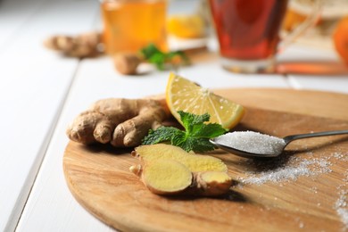 Photo of Ginger slices, lemon, mint and spoon of sugar on white wooden table, closeup