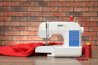 Photo of Sewing machine with fabric and craft accessories on wooden table against brick wall