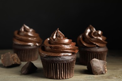 Photo of Delicious chocolate cupcakes with cream on wooden table against dark background