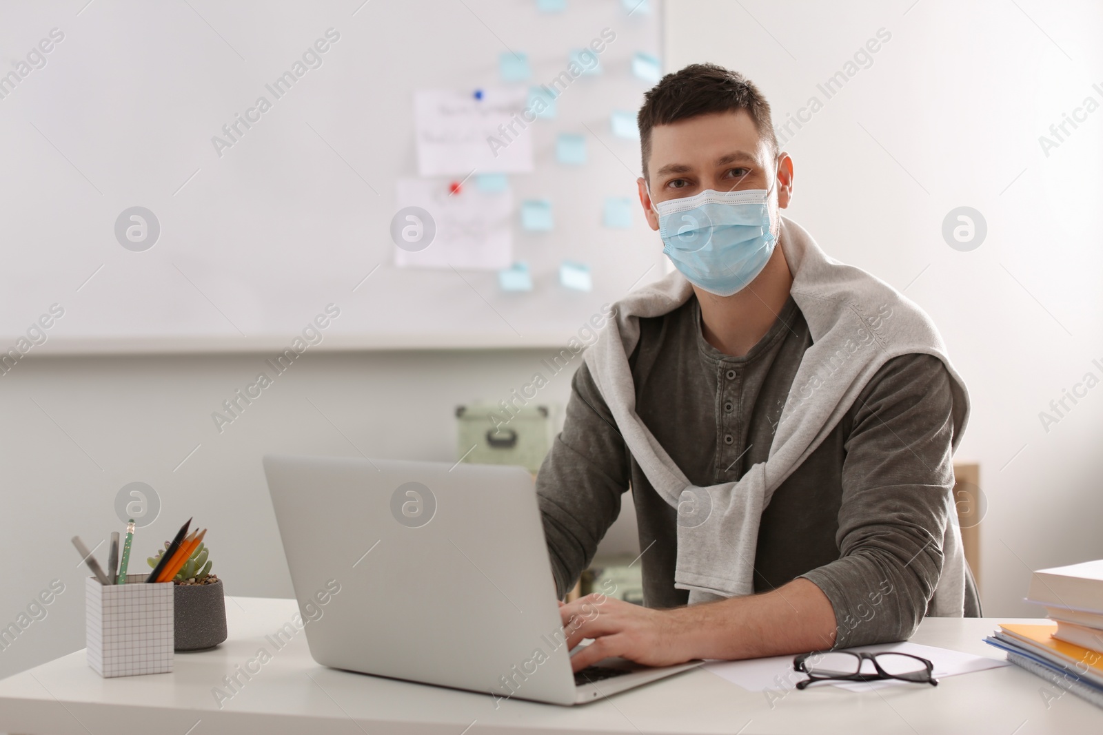 Photo of Teacher with protective mask and laptop sitting at desk in classroom. Reopening after Covid-19 quarantine