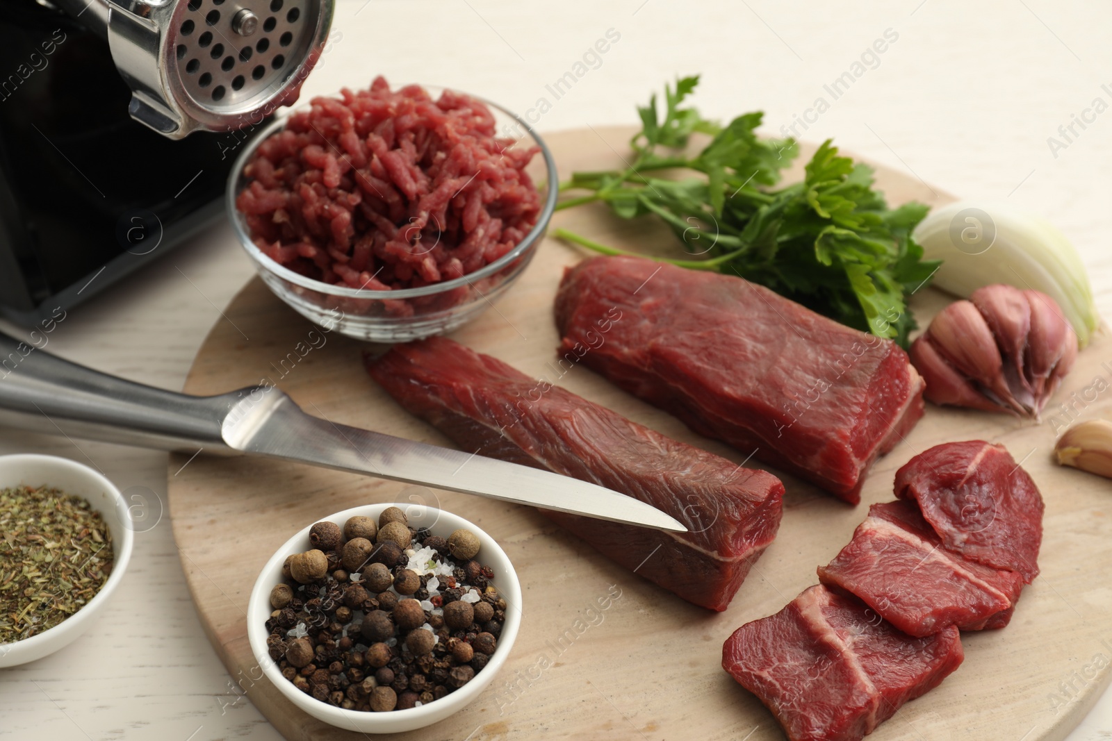 Photo of Meat grinder, beef, onion, garlic, parsley and spices on white wooden table, closeup