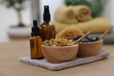 Photo of Bottles of essential oils, bowls with dry flowers and natural sponge on light wooden table, closeup. Spa therapy