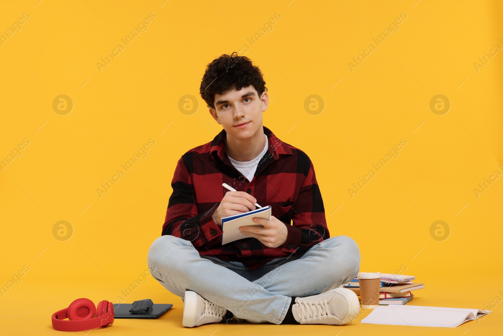 Photo of Portrait of student with notebook and stationery sitting on orange background