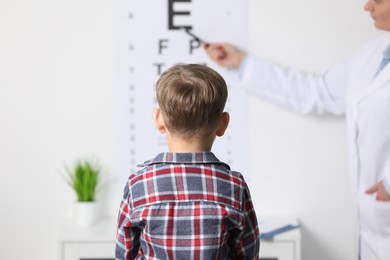 Photo of Ophthalmologist testing little boy's vision in clinic, back view