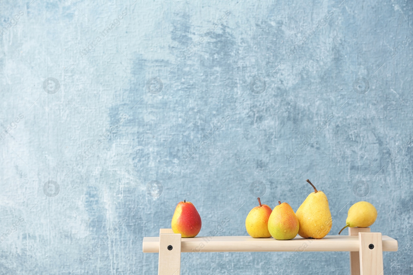 Photo of Ripe pears on wooden table against color background. Space for text