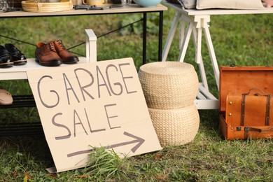 Sign Garage sale written on cardboard near tables with different stuff outdoors