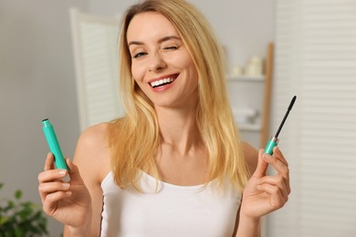 Beautiful happy woman with mascara in bathroom