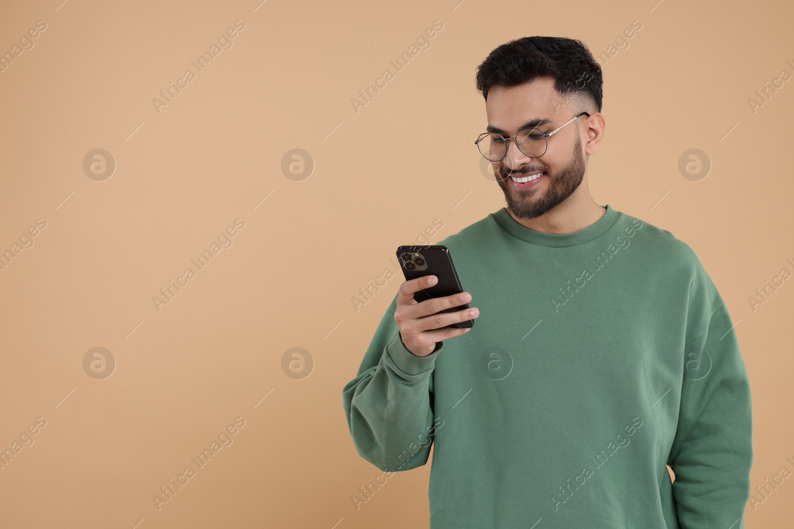 Photo of Happy young man using smartphone on beige background, space for text