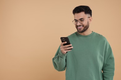 Happy young man using smartphone on beige background, space for text