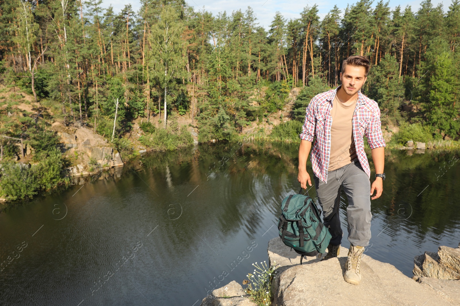 Photo of Young man on rock near lake and forest. Camping season