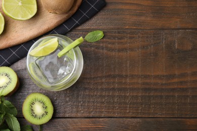 Glass of refreshing drink with cut kiwi and lime on wooden table, flat lay. Space for text