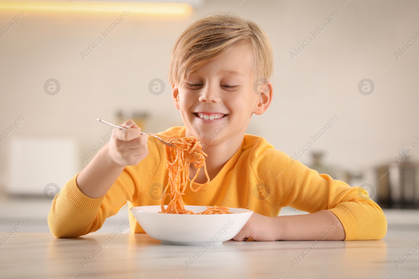 Photo of Happy boy eating tasty pasta at table in kitchen