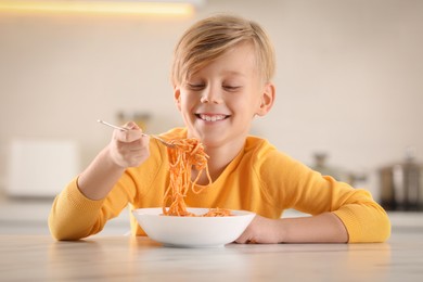 Photo of Happy boy eating tasty pasta at table in kitchen