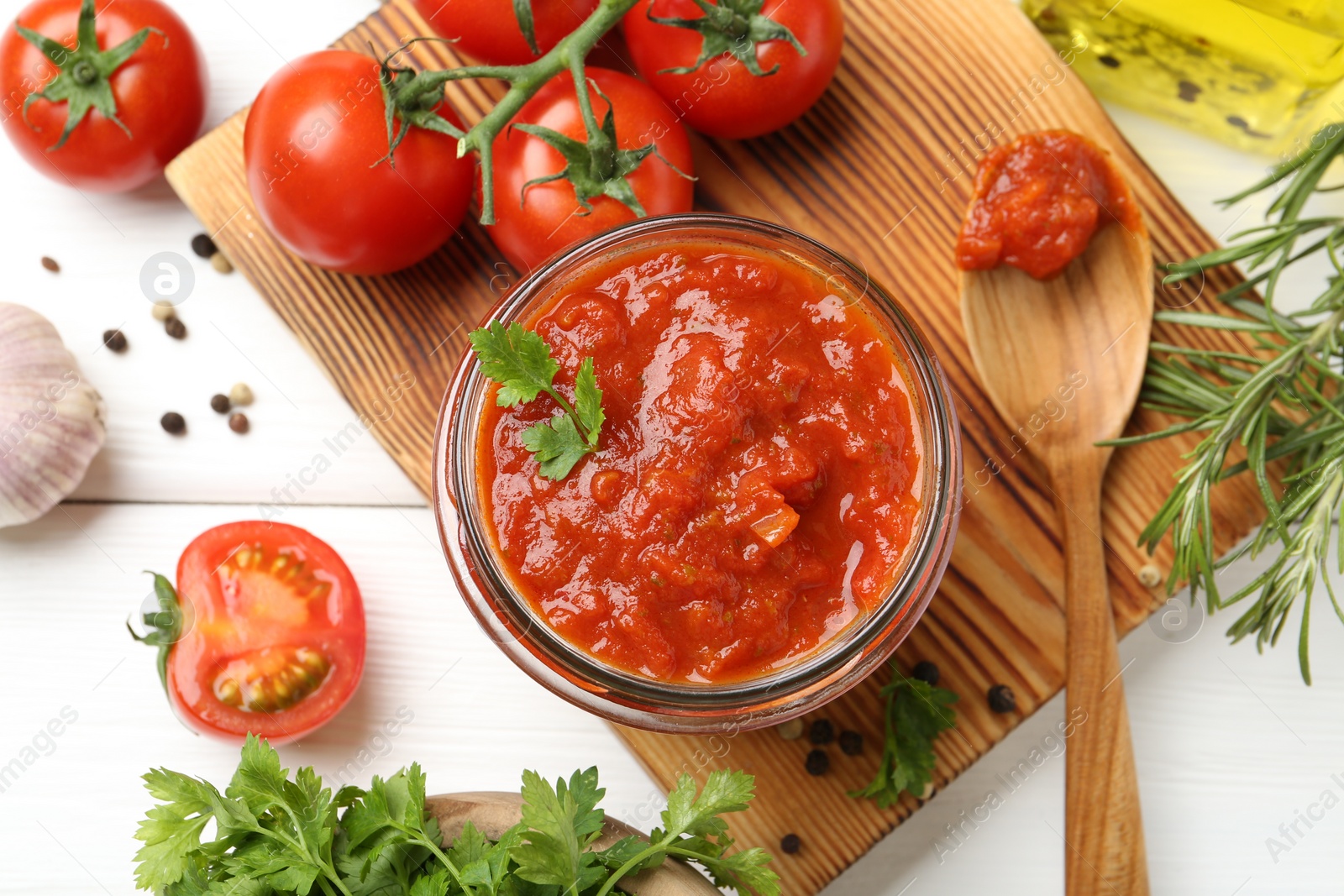 Photo of Homemade tomato sauce in jar, spoon and fresh ingredients on white wooden table, flat lay