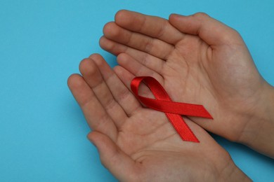 Photo of Little girl holding red ribbon on blue background, closeup. AIDS disease awareness