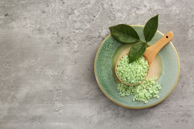 Aromatic sea salt and green leaves on grey textured table, top view. Space for text