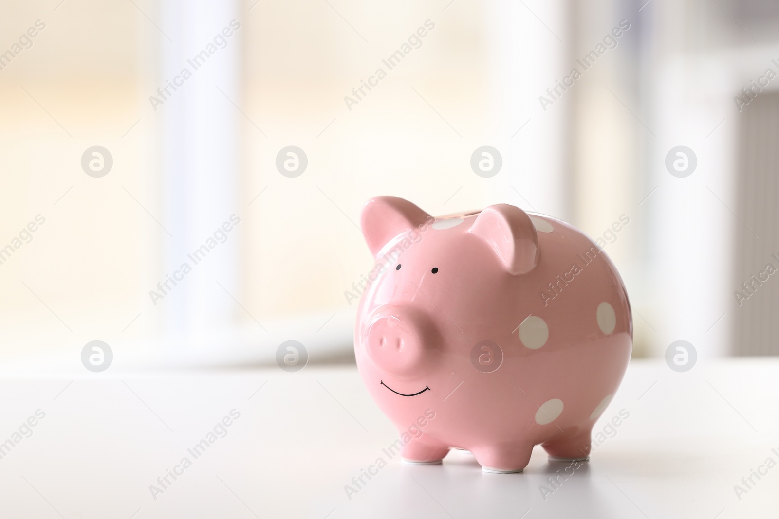 Photo of Piggy bank on table against blurred background. Space for text