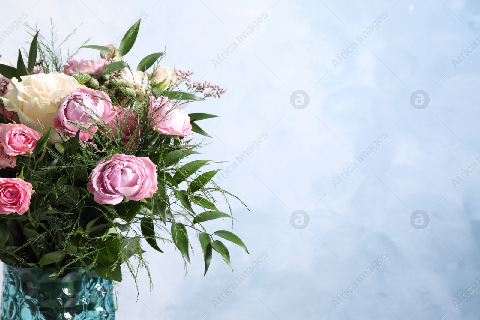 Photo of Beautiful bouquet with roses on light blue background, closeup. Space for text