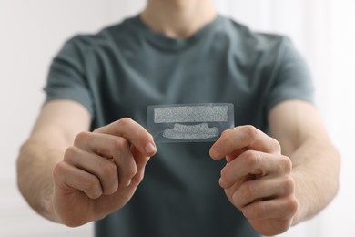 Photo of Young man with whitening strips on light background, closeup