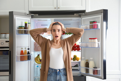 Photo of Emotional young woman near open refrigerator in kitchen